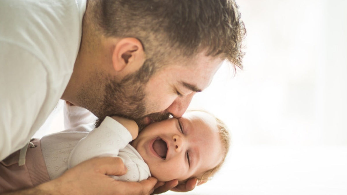 Dad lying on the floor kissing his laughing baby's cheek