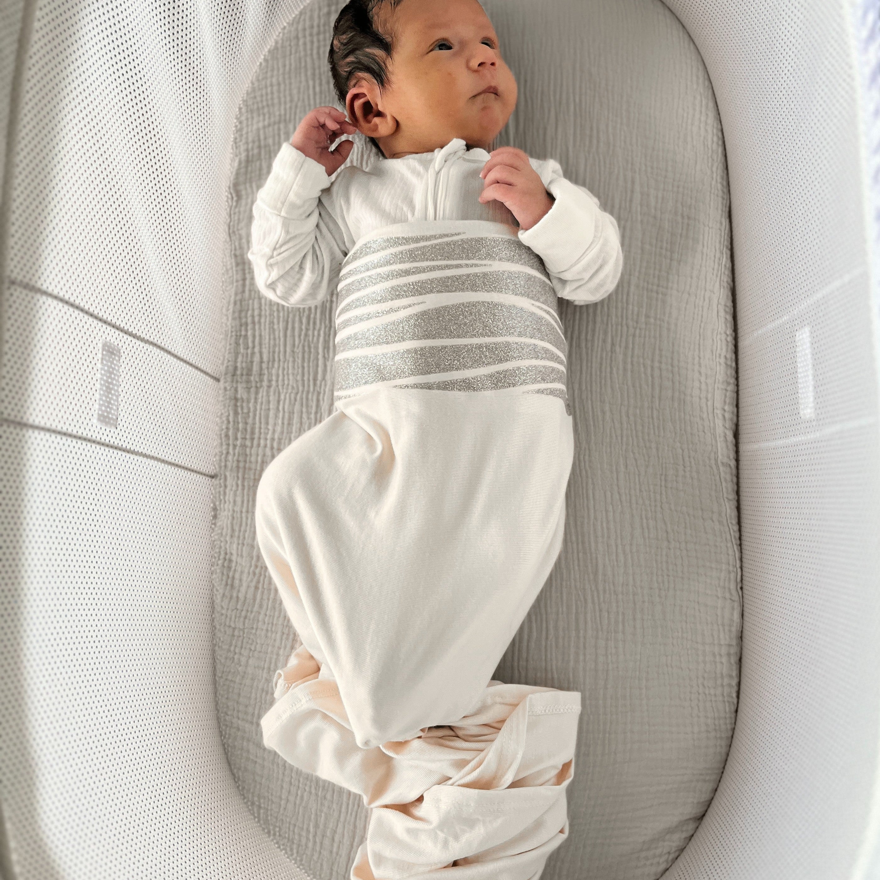 Newborn baby in a white outfit lying in a gray crib