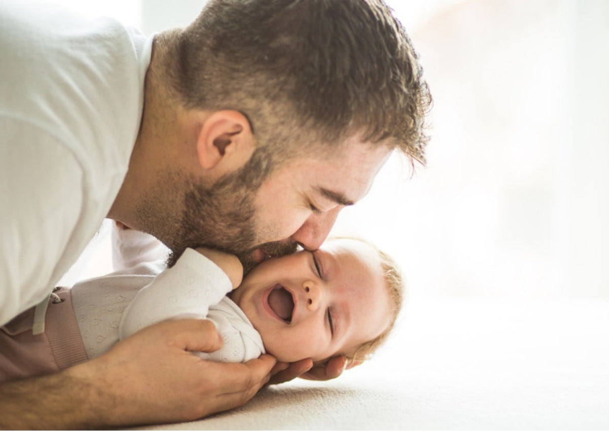 Dad lying on the floor kissing his laughing baby's cheek