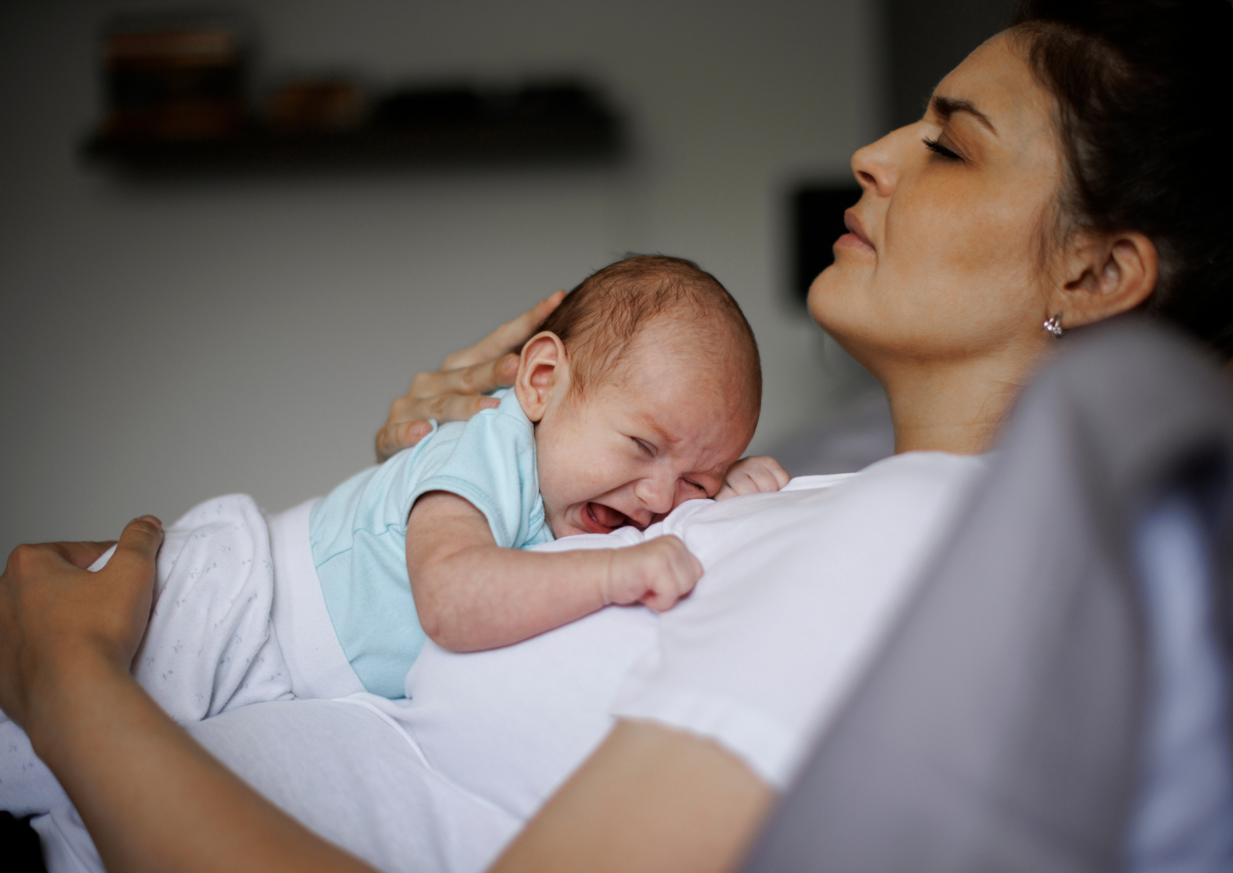 Woman lying on a bed with a baby crying on her chest