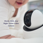A baby in white clothes lies on a soft surface next to a night vision video camera, with the text Works With Any Night Vision Video Camera displayed beside the camera.