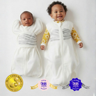 Newborn baby in a Sleep of Mind swaddle and a 5 month old baby in a Sleep of Mind sleep sack, both laying on a white surface side by side