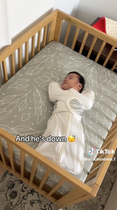 Baby in a white swaddle sleeping in a crib with a light-colored mattress.