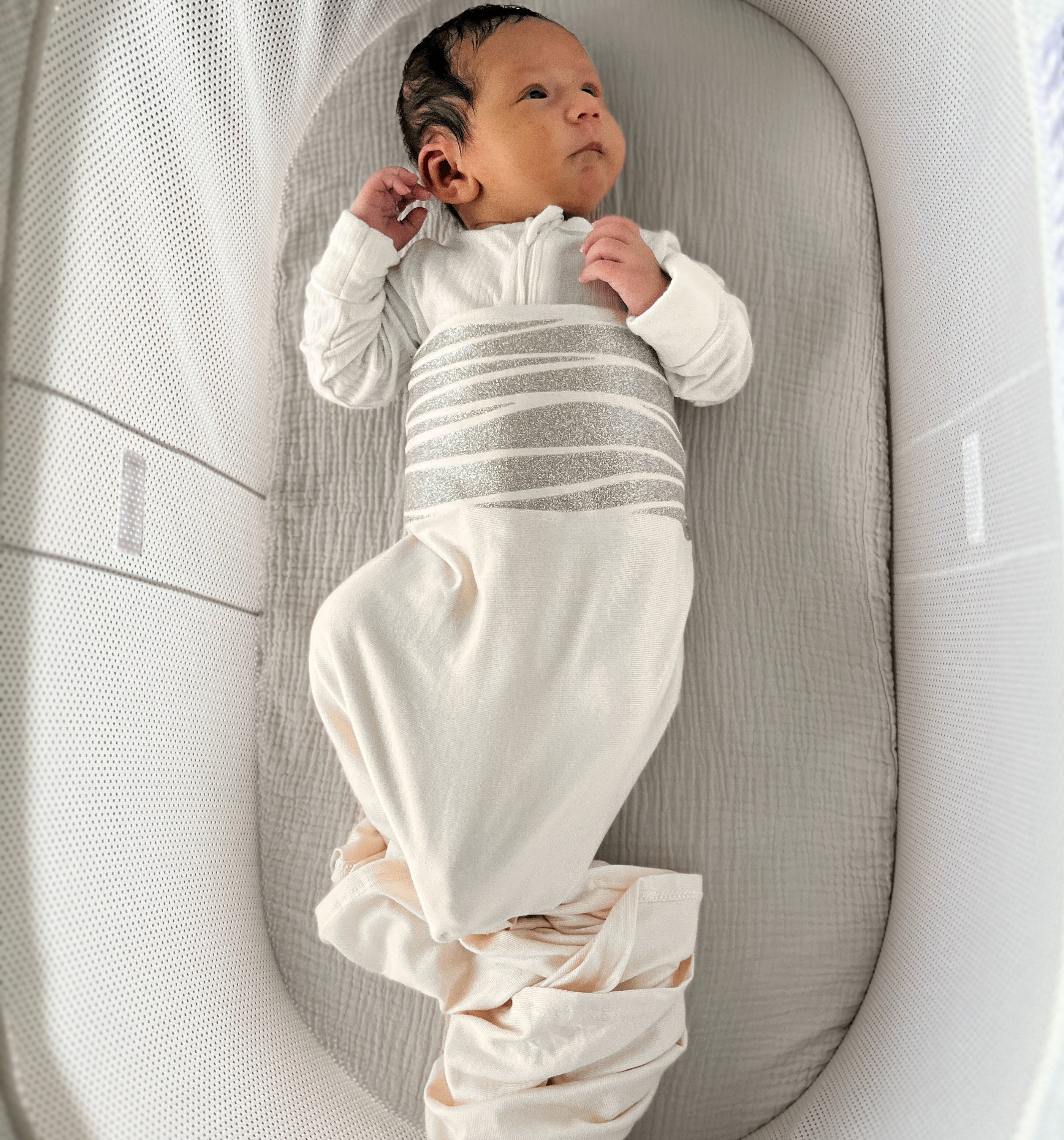 Newborn baby in a white outfit lying in a gray crib