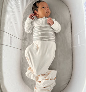 Newborn baby in a white outfit lying in a gray crib