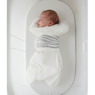 Newborn baby swaddled in a white and gray striped blanket lying on a white crib.